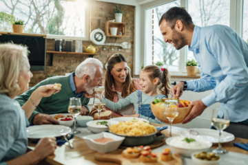 Eine Familie sitzt zusammen am Esstisch. Die Mutter serviert