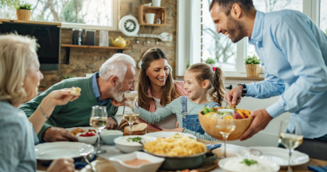 Eine Familie sitzt zusammen am Esstisch. Die Mutter serviert